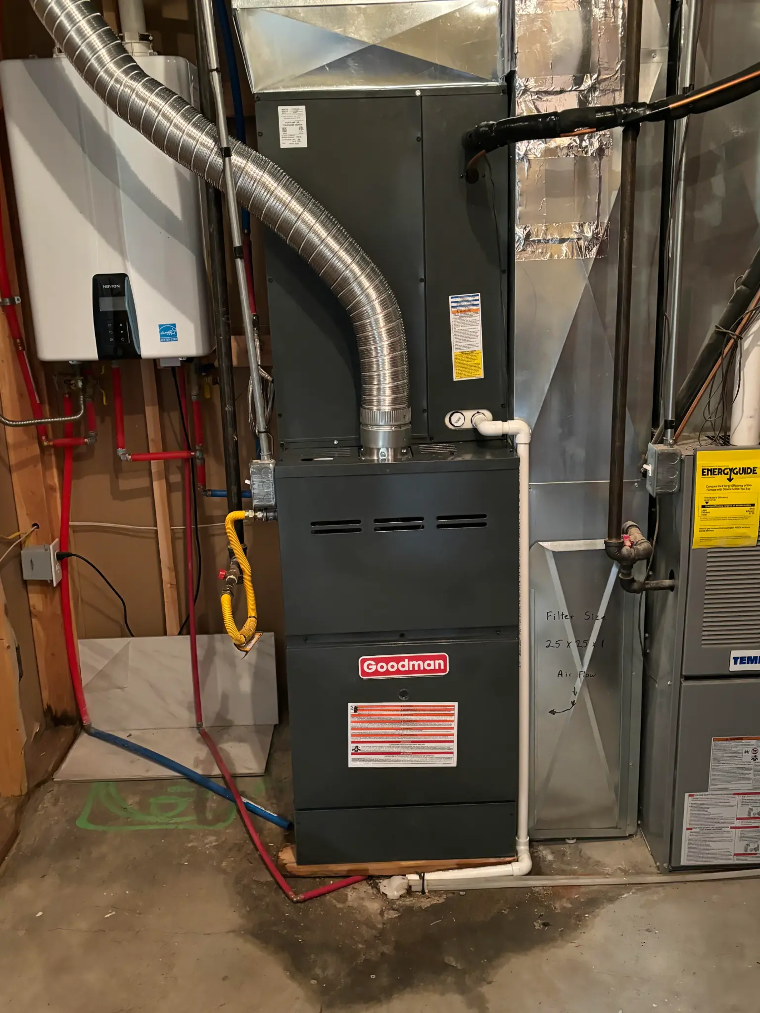 Goodman furnace installed in a basement mechanical room in Hurricane, Utah, alongside a tankless water heater with flexible exhaust duct and EnergyGuide label visible