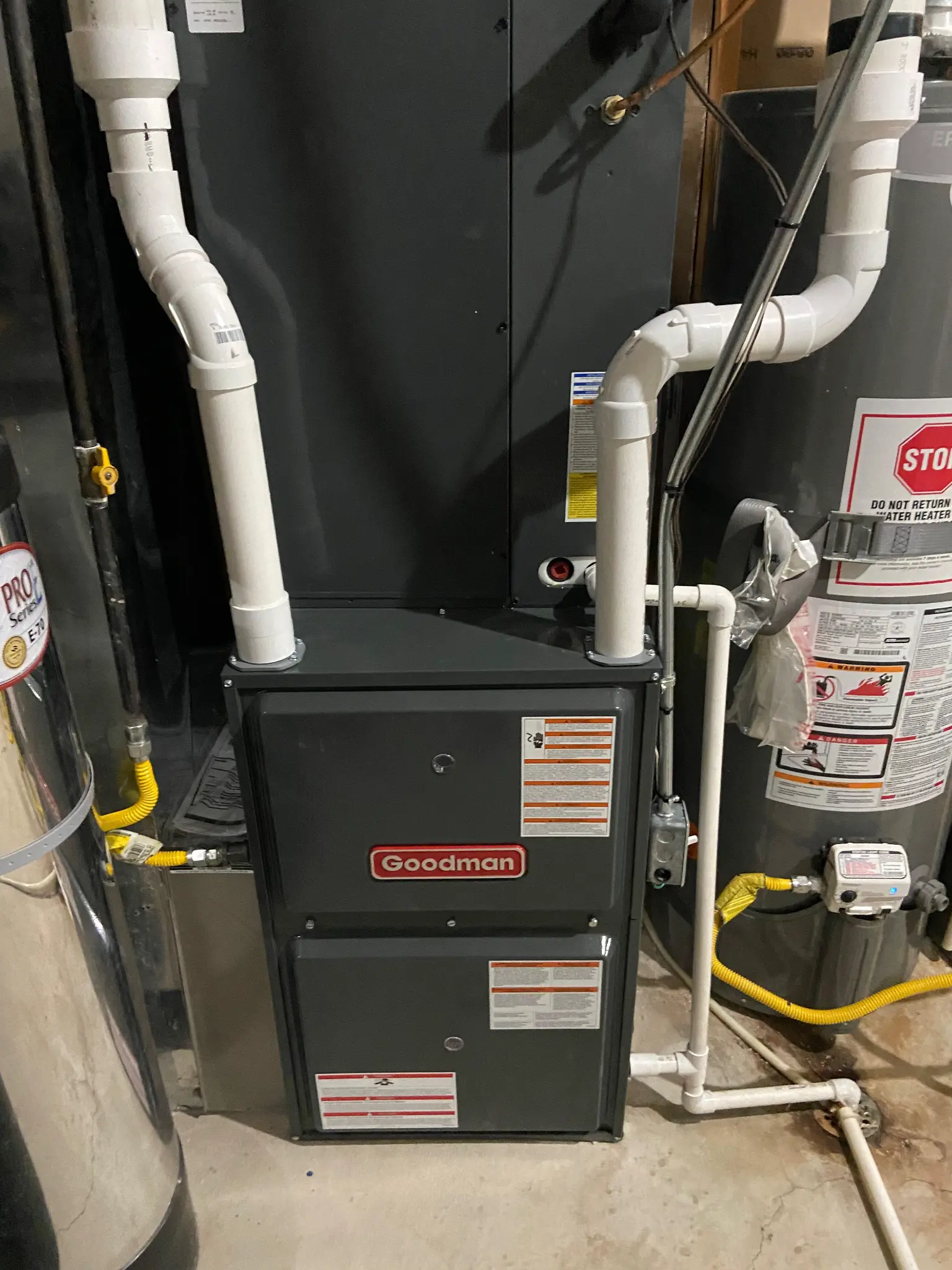 Goodman high-efficiency furnace installed in a tight utility room next to a water heater in Washington, Utah, with yellow CSST gas lines and PVC venting