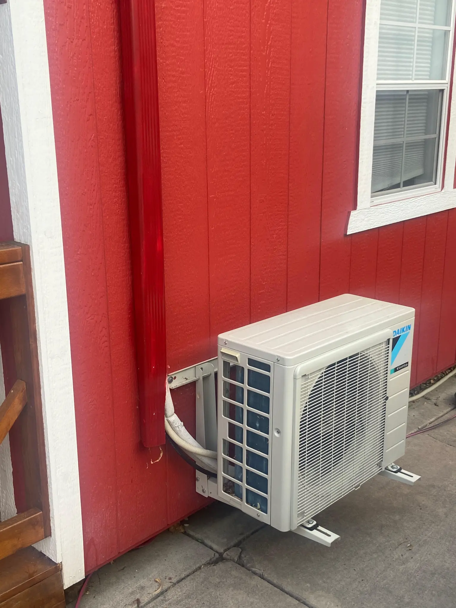 Daikin outdoor mini-split condenser mounted on brackets against red board-and-batten siding of a detached workshop in St. George area